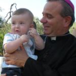 Con immenso piacere, invio la foto inedita (non l'ha mai vista neanche Don Gino) che ritrae Don Gino e Davide, mio figlio di 7 mesi, nell'agosto del 2009, quando al termine della messa da lui presieduta, in occasione della Festa Patronale, presso il casale della Madonna di Corsignano in Giovinazzo, Don Gino si trattenne, come suo solito, con i fedeli presenti per la rituale colazione.
Quel giorno, Don Gino conosceva ufficialmente mio figlio e fu una grande emozione, perché Davide non solo non pianse per il distacco dalla mamma ma sembrò gradire particolarmente il suo abbraccio al punto che impugnò la sua croce pettorale come fosse un nuovo gioco....
La scena destò lo stupore e il sorriso di molti tanto che una mia amica fotografò quella scena colma di tenerezza. D'altra parte rimane nel cuore di tutti il forte legame di Don Gino con i bambini... Durante la processione della Madonna di Corsignano, Don Gino era sempre seguito dai bambini che si avvicinavano a lui per ricevere la sua carezza...
Ci rimane nel cuore il suo dolce sorriso che è la traduzione visibile del suo amore per la nostra Chiesa diocesana.
Giulia Carlucci